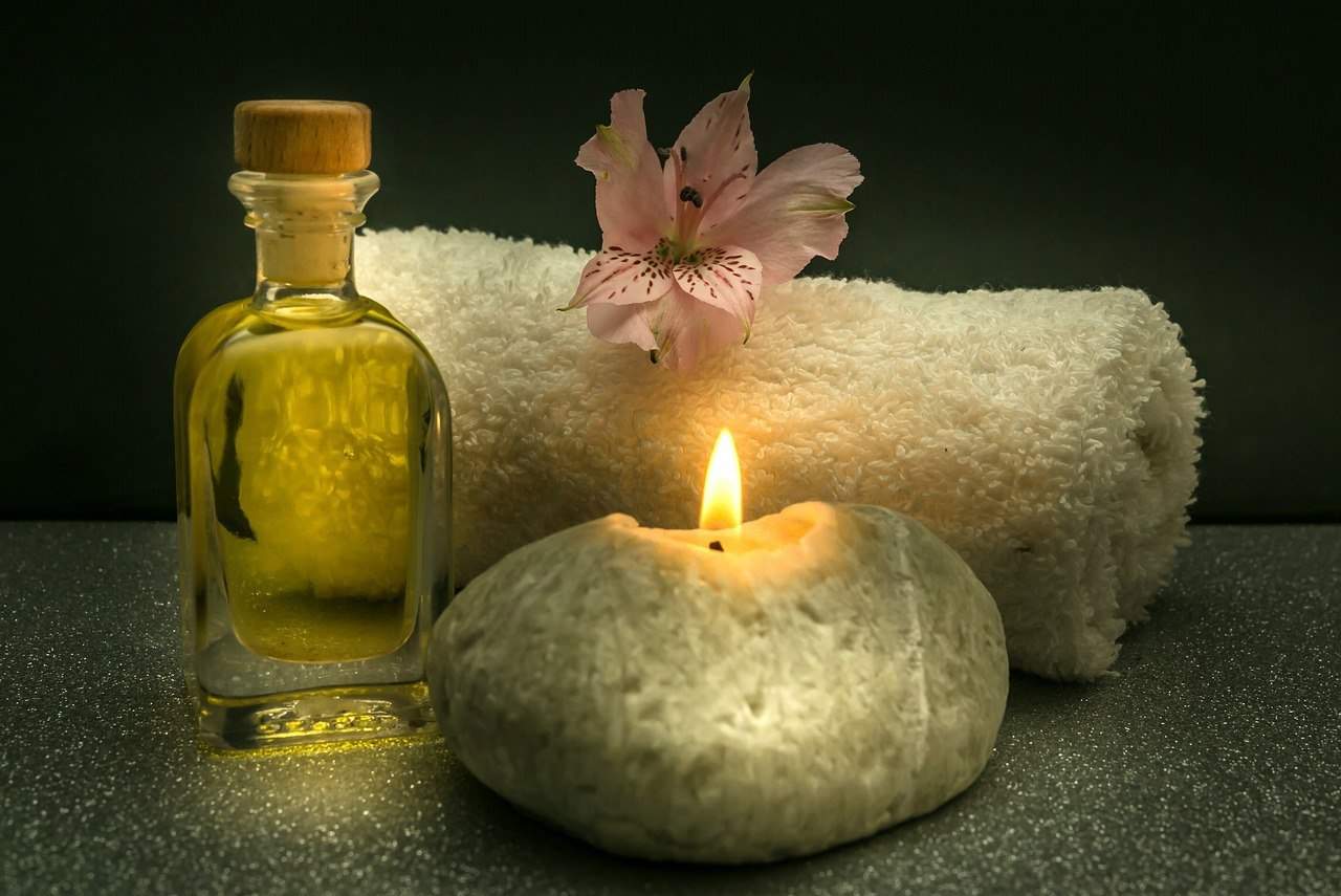 bottle of massage oil, lit candle, and towel - ready for a massage at home
